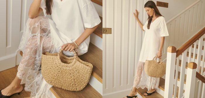 Frau in weißem Kleid mit Spitzenabschluss, die eine geflochtene Handtasche hält und an einer Innentreppe steht.