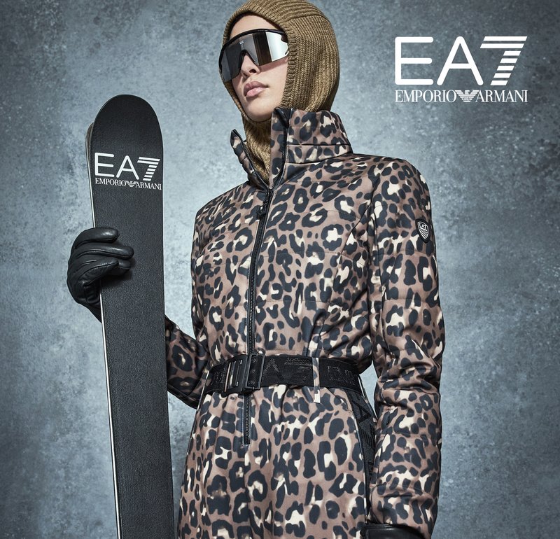 Chaqueta de esquí con estampado de leopardo y cintura con cinturón, combinada con guantes negros y un esquí. El modelo lleva gafas de sol y un pañuelo de punto en la cabeza.