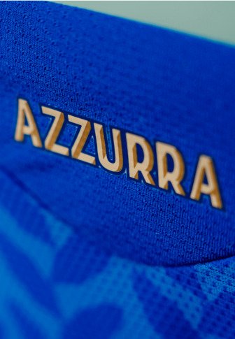 Zbliżenie na niebieski teksturowany materiał z wyhaftowanym złotymi literami słowa "AZZURRA".