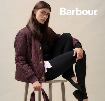 Bordeaux farbige gesteppte Jacke mit Messingknöpfen, schwarze Leggings und flachen Schuhen. Modell sitzt auf einem Hocker, hellen Hintergrund.
