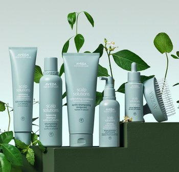 Vijf Aveda hoofdhuidverzorgingsproducten in gedempte groene verpakkingen: exfoliërende behandeling, balancerende shampoo, conditioner, verfrissende spray en hoofdhuidserum.