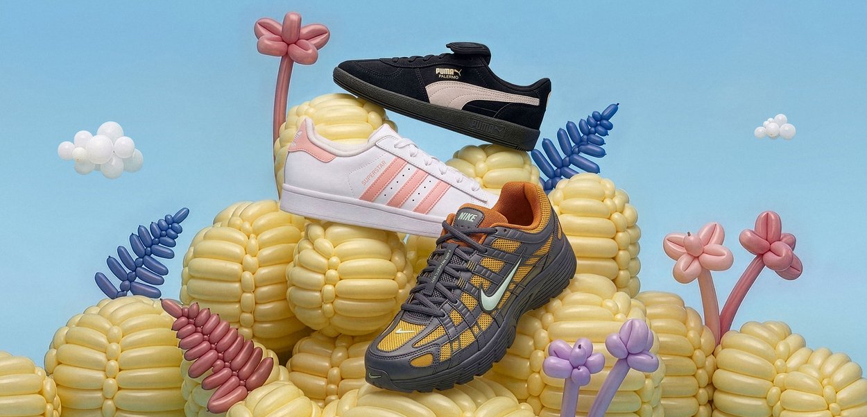 Tre sneakers — sorte Puma, hvide Adidas med lyserøde striber og grå Nike med orange accenter — ligger på en bunke gule ballonklumper formet som majs.