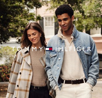 Zwei Modelle gehen nebeneinander, eines trägt einen karierten Mantel und einen gerippten beigen Pullover, das andere in einer Jeansjacke und einem gestreiften Hemd.