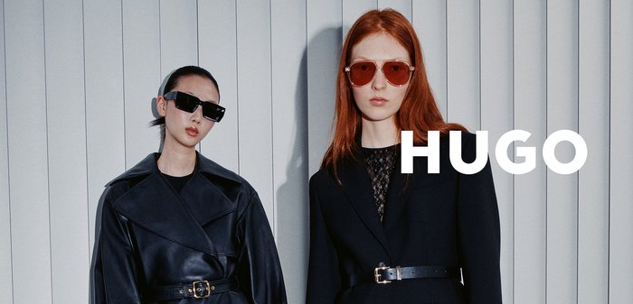 Deux mannequins portent des tenues à la mode : l'un dans un manteau en cuir noir, l'autre dans un blazer noir avec un haut en dentelle, tous deux portant des lunettes de soleil.