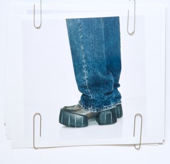 Persona che indossa jeans blu e scarpe platform nere con suole spesse, in piedi su una superficie bianca.