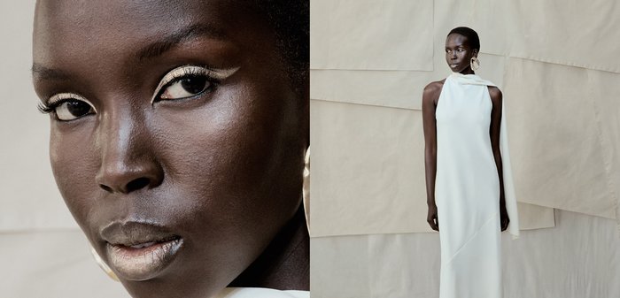 Femme à la peau foncée avec un maquillage audacieux blanc sur les yeux, portant une robe blanche dos nu et de grandes boucles d'oreilles, sur un fond beige.