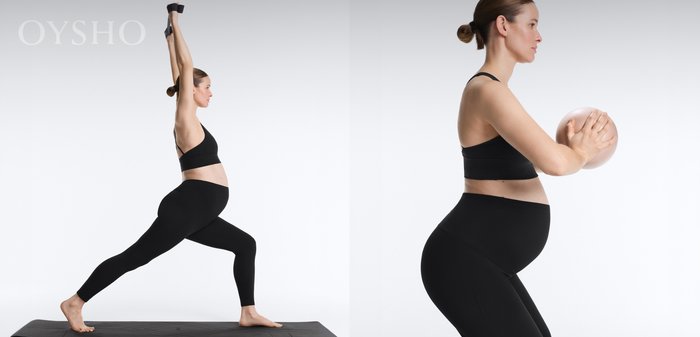 Pregnant woman in black sportswear performs a yoga warrior pose with arms raised above head on a black mat.