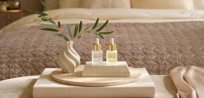 Bouteille en verre contenant un liquide jaune clair avec un compte-gouttes transparent. L'étiquette indique "booster naturel BAKUCHIOL teint et élasticité". Accents argentés.