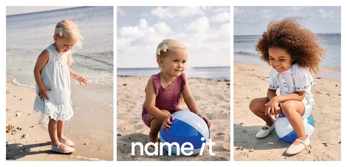 Mali otroci se igrajo in hodijo po peščeni plaži blizu vode, držijo in sedijo na modro-beli plažni žogi.