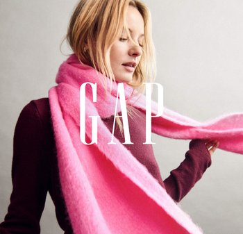 Lyserød uld tørklæde draperet omkring halsen med en blød tekstur. Modellen bærer en vinrød langærmet top. Brandet "GAP" er tydeligt vist.