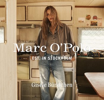 Kobieta z rozpuszczonymi włosami, ubrana w brązową kurtkę i niebieskie dżinsy, stoi w przytulnej kuchni kampera obok kuchenki i stołu jadalnego.