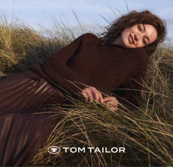 Brauner Strickpullover mit lockerer Passform, kombiniert mit einem plissierten braunen Rock, vor einer grasbewachsenen Fläche unter klarem Himmel.