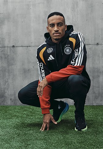 Czarny i czerwony dres z kapturem w białe i pomarańczowe paski, z logo na piersi i rękawach. Noszony z czarnymi spodniami i kolorowymi sneakersami.