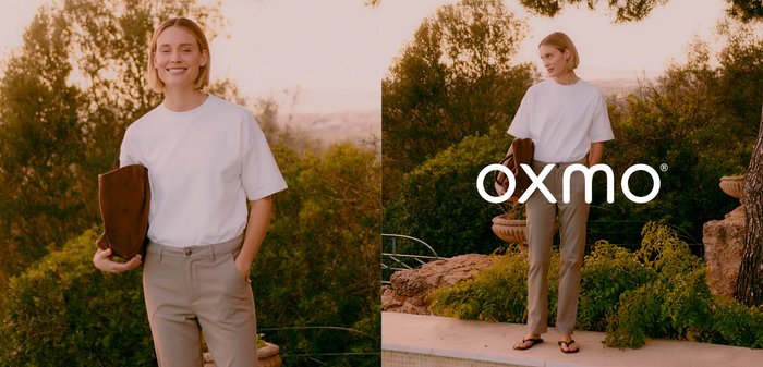 Frau lächelnd und am Pool stehend, trägt ein weißes T-Shirt, beige Hose, Flip-Flops, hält eine braune Clutch, mit Grün im Hintergrund.