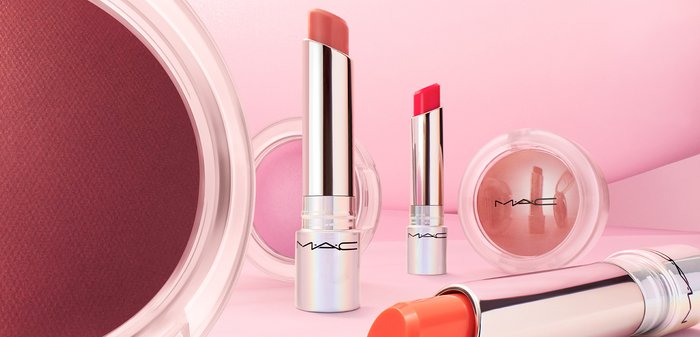 Cosmetici MAC con tre tubetti di rossetto in diverse tonalità di rosa e corallo, con tappi metallici lucidi, affiancati da una cipria rotonda.