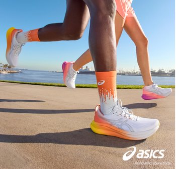 Twee hardlopers in witte en oranje Asics-schoenen joggen op een pad langs het water onder een heldere blauwe lucht, waarbij beweging en atletische activiteit worden getoond.