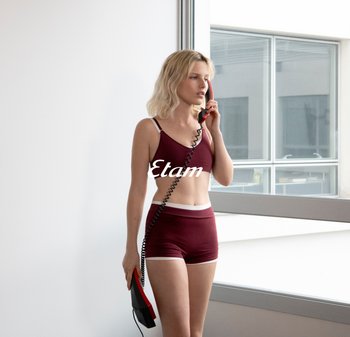 Set di reggiseno e pantaloni corti color bordeaux con rifiniture bianche. Tessuto morbido, design aderente. Soggetto che tiene in mano un telefono retro rosso, in piedi vicino a una grande finestra.