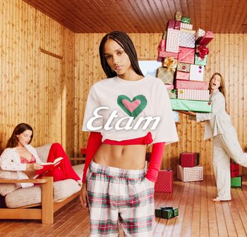 Weißes, kurzes T-Shirt mit einem grünen und pinken Herzdesign, kombiniert mit karierten Schlafanzughosen. Holzuntergrund und Weihnachtsgeschenke im Blickfeld.