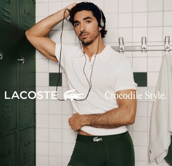 Mężczyzna w białej koszulce polo i zielonych bokserkach z logo krokodyla, stojący w szatni z nausznikami na uszach.