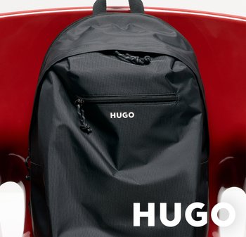 Mochila negra de la marca HUGO con bolsillo frontal con cremallera, descansando sobre una superficie roja y brillante.
