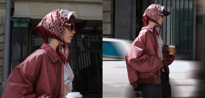 Sciarpa rossa stampata, giacca bomber borgogna over size, top bianco con borchie, jeans scuri, in mano una tazza di caffè, occhiali da sole che accentuano il look.