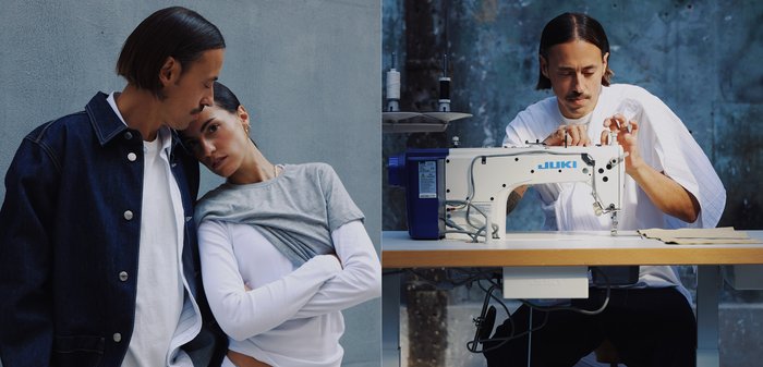 Jeansjacke mit silbernen Knöpfen, grauem Oberteil und weißem Hemd. JUKI-Nähmaschine auf einem Holztisch, Stoffstücke und Garnrollen sichtbar.