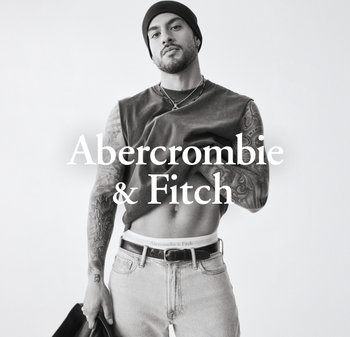 Model w ciemnej bezrękawnikowej koszulce i jasnoniebieskich dżinsach, eksponujący tatuaże. Na głowie czarna czapka beanie i pasek Abercrombie & Fitch.