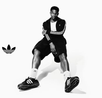 Czarne sportowe sneakersy z białymi paskami, zestawione z czarną kurtką na zamek z trzema paskami i czarnymi szortami. Białe skarpetki dodają kontrastu.