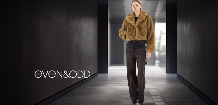 Καφέ ψεύτικο γούνινο cropped jacket με γιακά σε μανιά, συνδυασμένο με μαύρα τζιν ψηλής μέσης και μαύρες γόβες σε έναν μοντέρνο, μινιμαλιστικό χώρο.