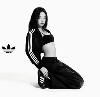 Ensemble de sport noir comprenant une veste courte avec des rayures blanches, un soutien-gorge de sport noir et un pantalon noir ample. Chaussures noires avec des accents de rayures.