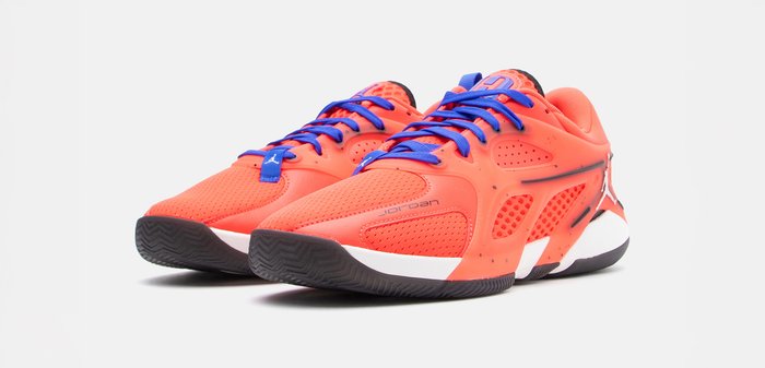 Φωτεινά πορτοκαλί παπούτσια Jordan χαμηλού τύπου με μπλε κορδόνια, μαύρες σόλες και λευκές ενδιάμεσες σόλες, ελαφρώς γωνιασμένα προς τα δεξιά σε λευκό φόντο.