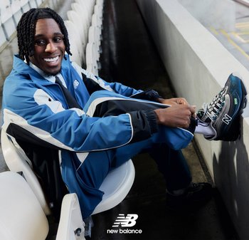 Sneaker con tomaia texturizzata blu scuro, accenti blu chiaro e dettagli riflettenti; abbinato a un tuta da corsa blu coordinata con strisce bianche.