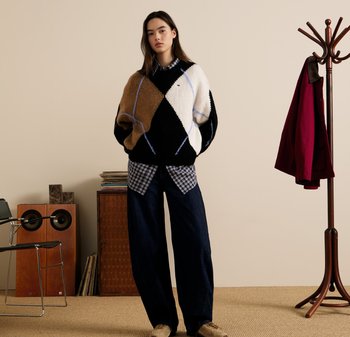 Gruba sweter w brązowym, białym i czarnym kolorze z diamentowym wzorem; nałożony na niebieską koszulę w kratę; w zestawie z szerokimi ciemnymi dżinsami.