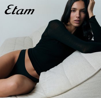 Vrouw in zwarte top met lange mouwen en ondergoed liggend op een witte, gestructureerde bank met het logo van "Etam" linksboven.