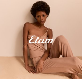 Beige Ripp-Loungewear-Set mit einem spitzenbesetzten Oberteil, das dünne Träger und lässig geschnittene Hosen hat. Sanfte Textur vor einem neutralen Hintergrund.