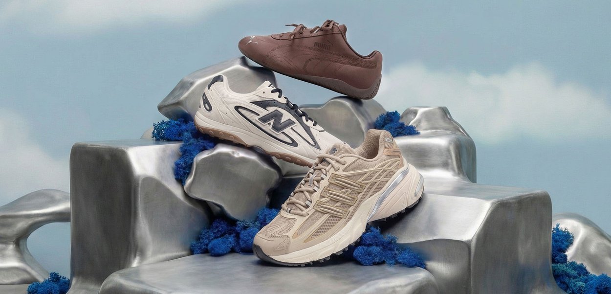 Tres zapatillas New Balance en marrón, blanco y beige expuestas sobre rocas plateadas metálicas con decoraciones azules similares al coral.