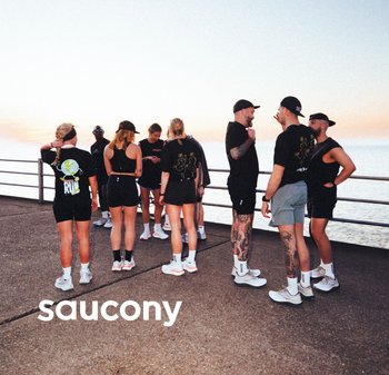 Groupe d'individus vêtus de t-shirts et de shorts de sport noirs, avec des chaussures blanches. L'arrière-plan présente une vue côtière au coucher du soleil.