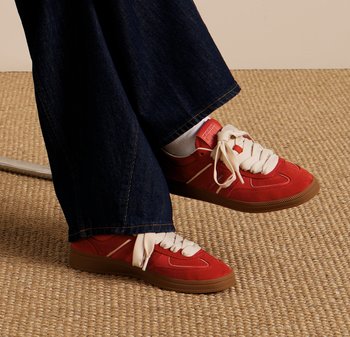 Baskets en daim rouge avec lacets blancs, dotées d'une semelle rembourrée, de bandes latérales et d'un logo sur le talon, portées avec un pantalon en denim noir.