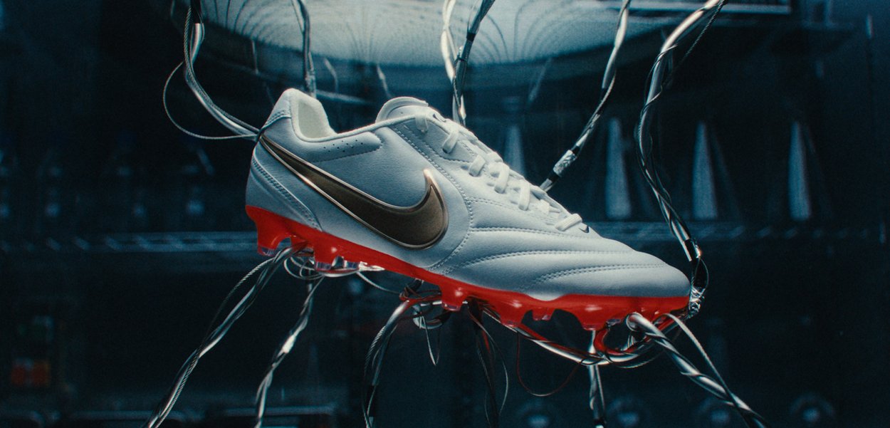 Valge ja punane Nike jalgpallikets, mis ripub mitme musta ja hõbedase kaabli küljes pimedas, tehnoloogilises keskkonnas.