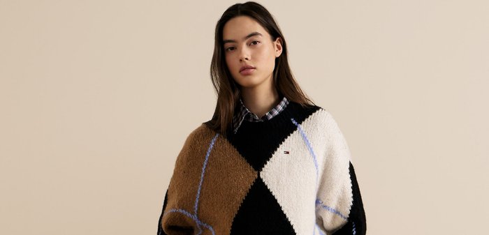 Maglione lavorato a maglia spesso in marrone, nero e bianco. Presenta forme a diamante con accenti blu e un logo sul petto. Tessuto con texture.