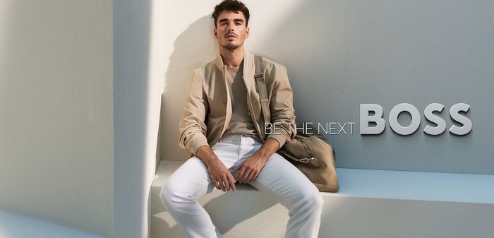 Jovem com casaco bege, calças brancas e sapatilhas sentado confiantemente nos degraus brancos ao lado do texto "Seja o próximo CHEFE."