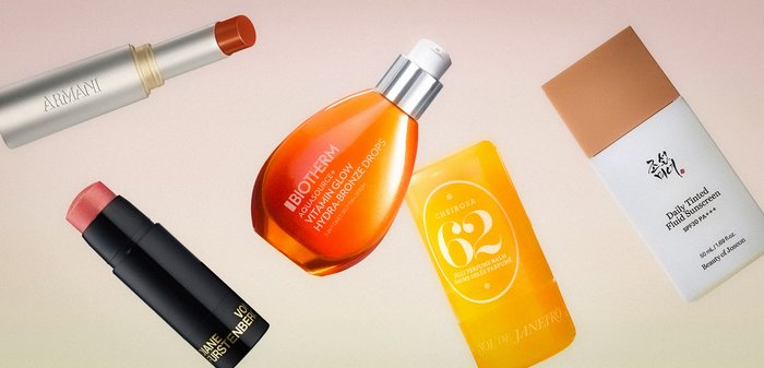 Læbestift, bronzedråber, tonet fugtighedscreme og to pindbalsam arrangeret på en lys overflade.