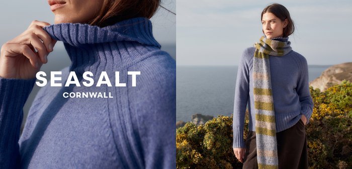 Svetle modrý žebrovaný rolák z měkké tkaniny, doplněný pruhovaným šálem v zelených a béžových odstínech. Přírodní přímořské pozadí.