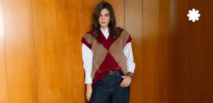 Chandail en argyle tricoté en beige et bordeaux, associé à une chemise blanche à boutons et un jean large bleu marine. Accessoires et chaussures marron.