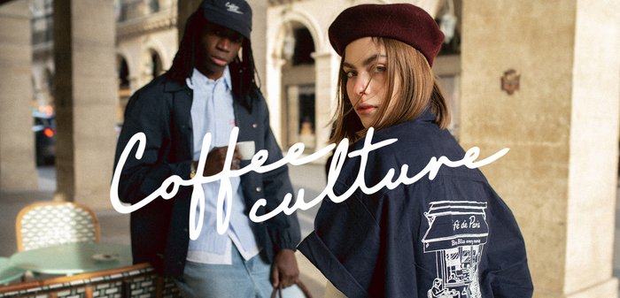 Dos personas en una cafetería al aire libre con tazas de café; una lleva una boina y una chaqueta con una ilustración de una cafetería y la superposición de texto "Cultura del café".