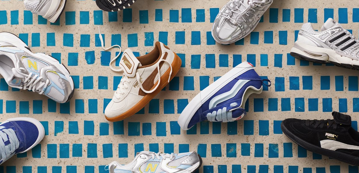 Varios zapatos deportivos informales en diferentes colores dispuestos sobre un suelo de baldosas con patrones de cuadros azules.