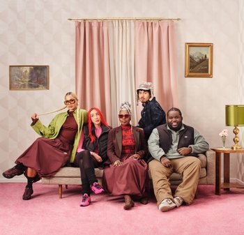 A diverse group of five individuals seated on a beige couch, wearing a mix of styled clothing, against a light pink wall with geometric patterns.
