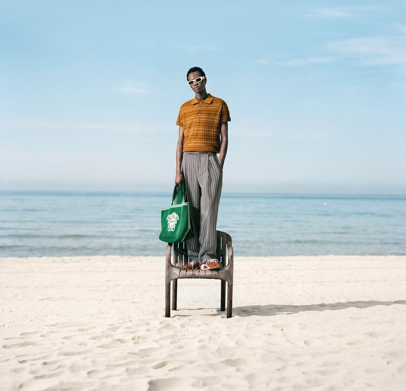 Persona con gafas de sol y ropa informal recostada en una tumbona amarilla en una playa de arena junto al mar bajo un cielo despejado.