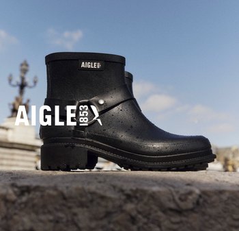Bottes en caoutchouc noires à la cheville avec surface texturée, détail de boucle et semelle crantée. Marque AIGLE visible sur le devant.