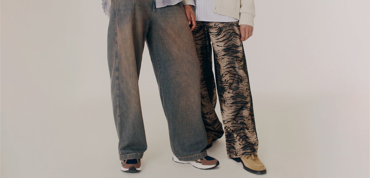 Jeans din denim cu picioare largi, de culoare albastru deschis, asociați cu pantaloni de imprimare animal în nuanțe de bej și negru. Ambele au o croială lejeră și texturi variate.